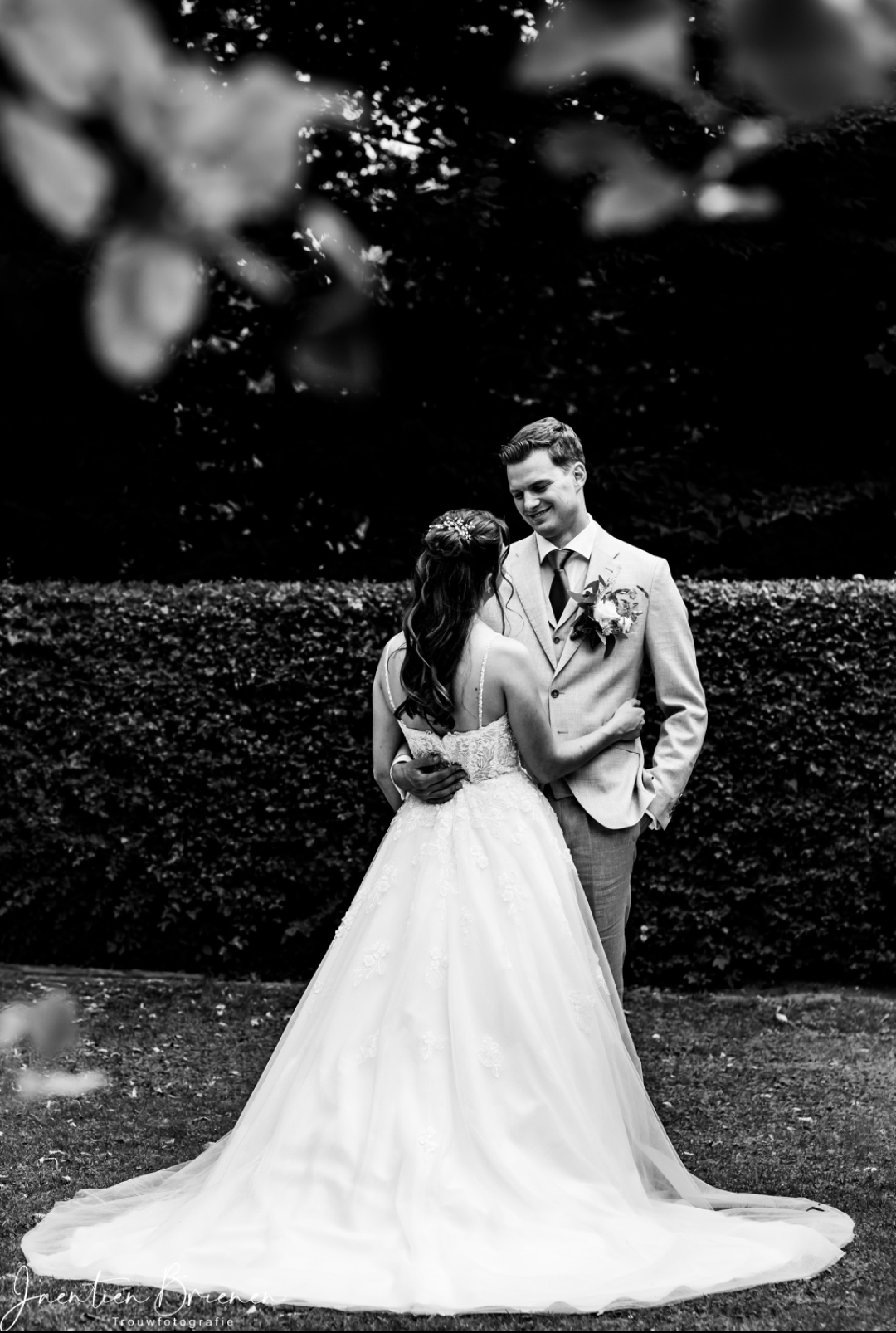 Real bride Melanie staat met haar partner in een tuin, in een A-lijn trouwjurk met kanten top en lange sleep